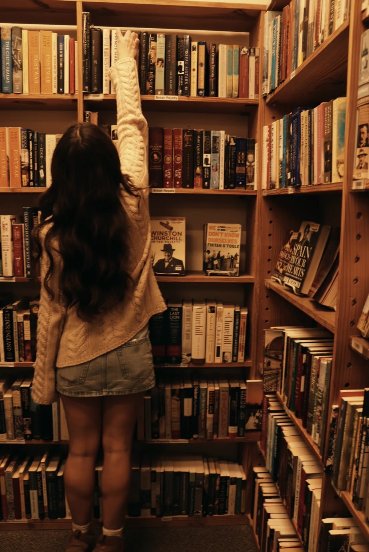 A woman reaching for a book in a warmly lit bookshop