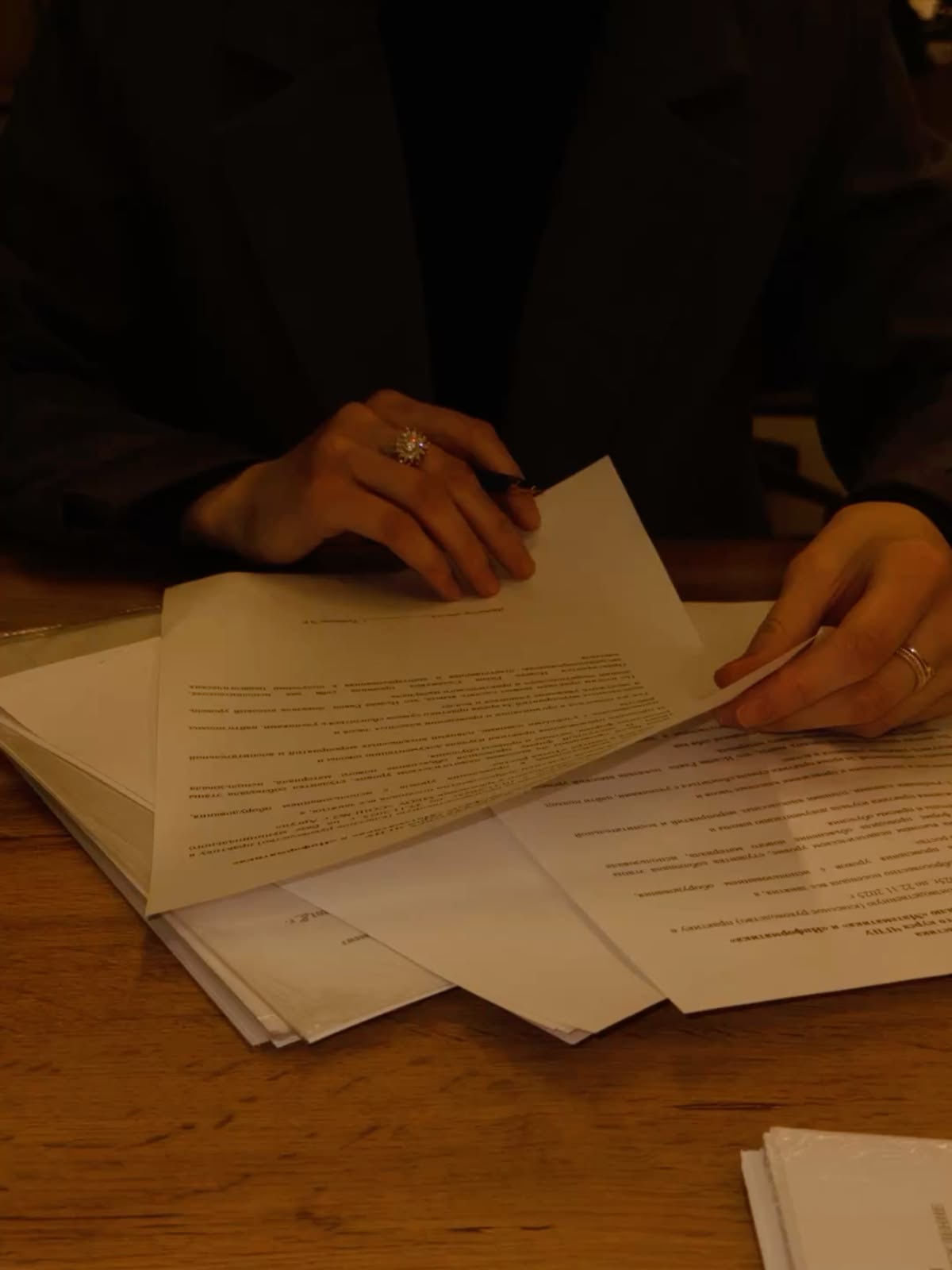 Moody dark photo of hands sorting through documents on a desk, warm candlelit work-in-progress atmosphere.