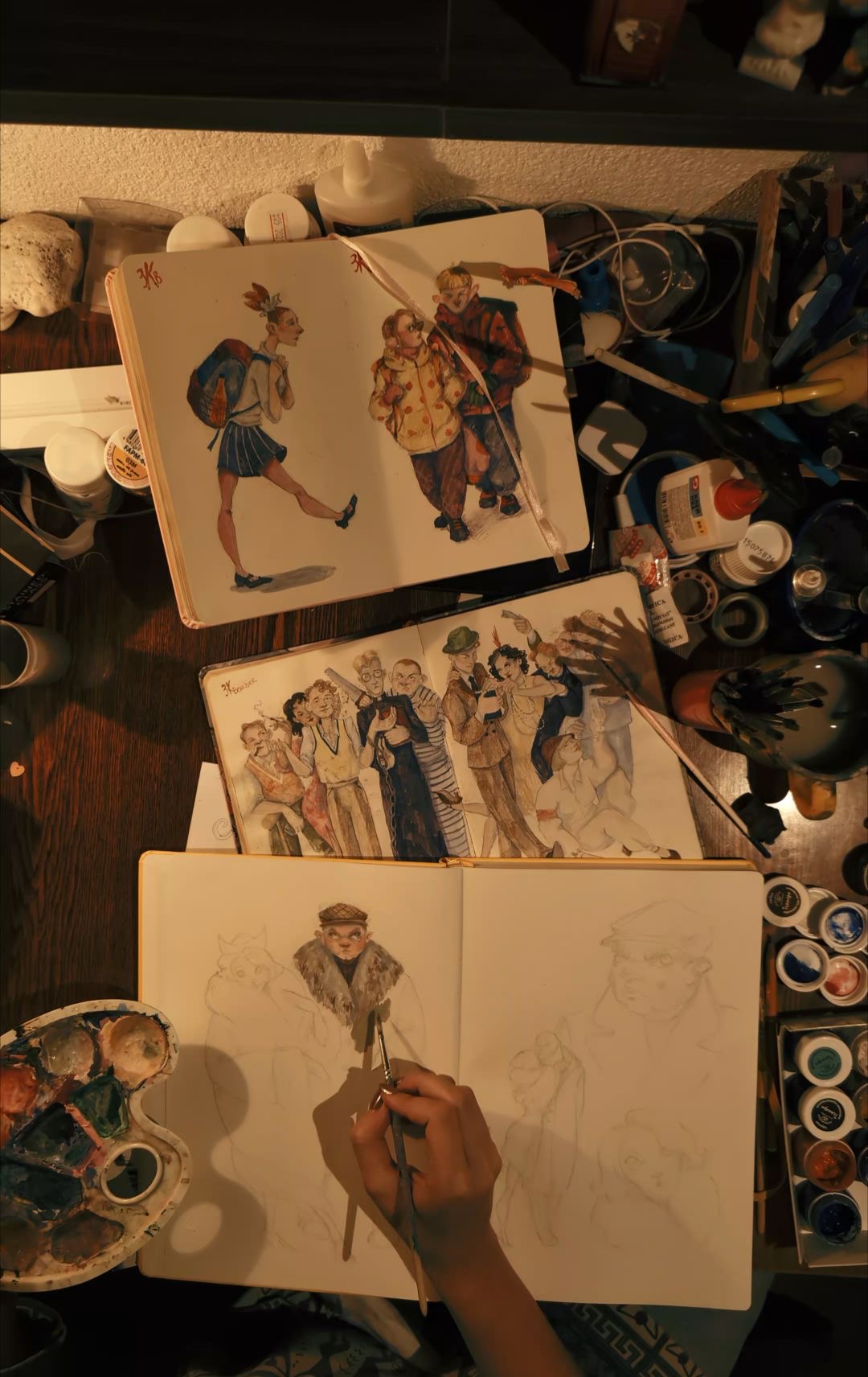 Overhead shot of an artist's sketchbooks and paints spread across a desk, chaotic creative energy, representing The Burnout.